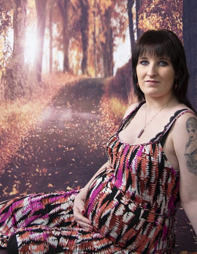pregnant lady in colourful dress seated in front of autumn trees & path