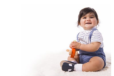 cute dark haired boy toddler seated on rug with orange toy in hands