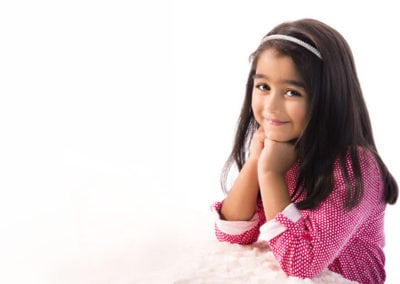 pretty young school girl in bright pink dotty dress smiling with her head resting on hands