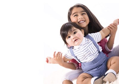 pre-school brother and sister sitting together happily holding hands aloft on floor, colour