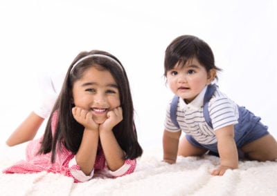 cute brother & sister lying & kneeling on rug smiling