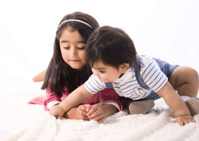 cute brother & sister sitting on rug looking down at object brother is trying to reach
