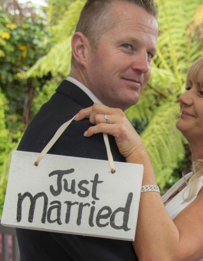 Bride & groom outdoors on deck in rain, just married sign